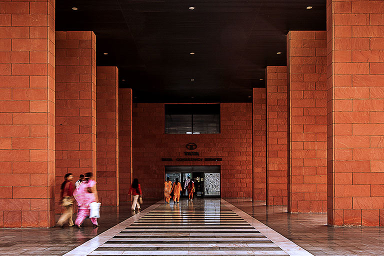 People walk down a long hall with tall brick columns on either side.
